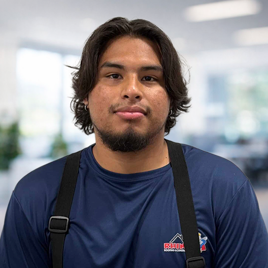 A young man with medium-length dark hair and a short beard wears a blue shirt with a 